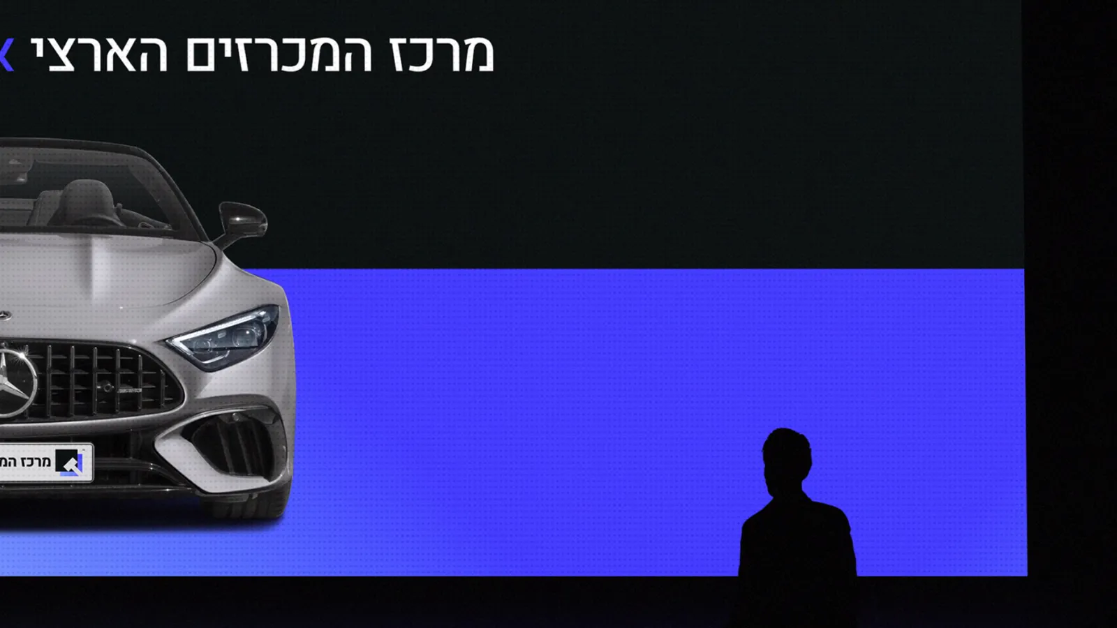 מכרז בשידור חי של מרכז המכרזים הארצי - מסך האולם מציג רכב מול קהל המשתתפים